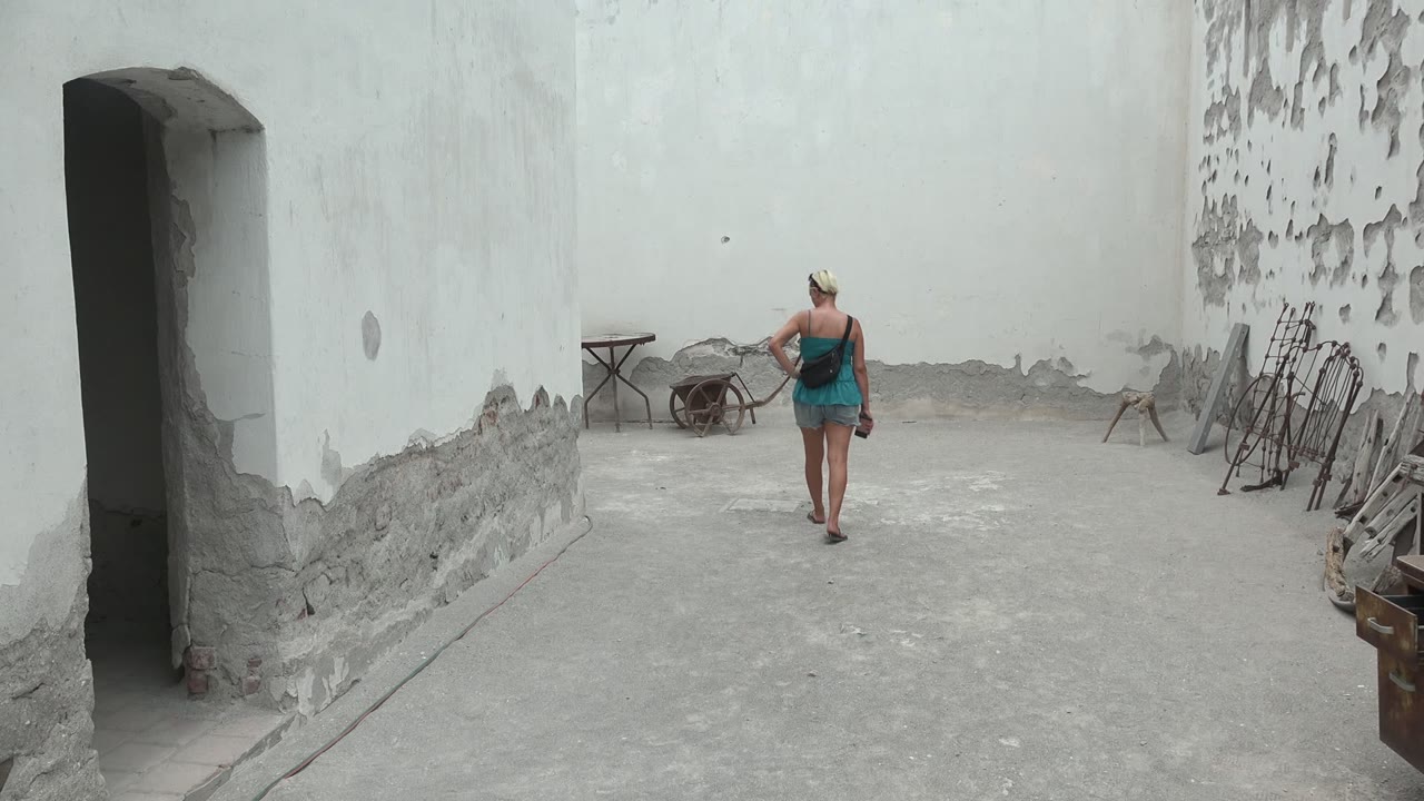 At the start of the Mulege, Mexico clip, a woman in a blue dress walks away from the camera across a gray concrete courtyard with a dark doorway on the left.
