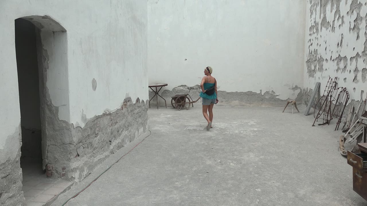Woman crossing the concrete courtyard near a wheelbarrow and table.
