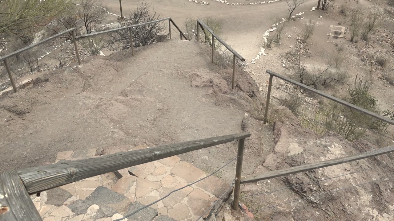 Opening view in Mulege, Baja California Sur shows a sandy stone stair landing, weathered railings, rocks, sparse shrubs, and no visible people.