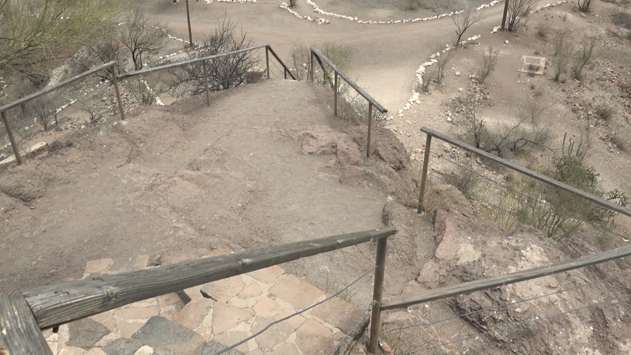 Desert stairway railings with sandy path and rocks below.