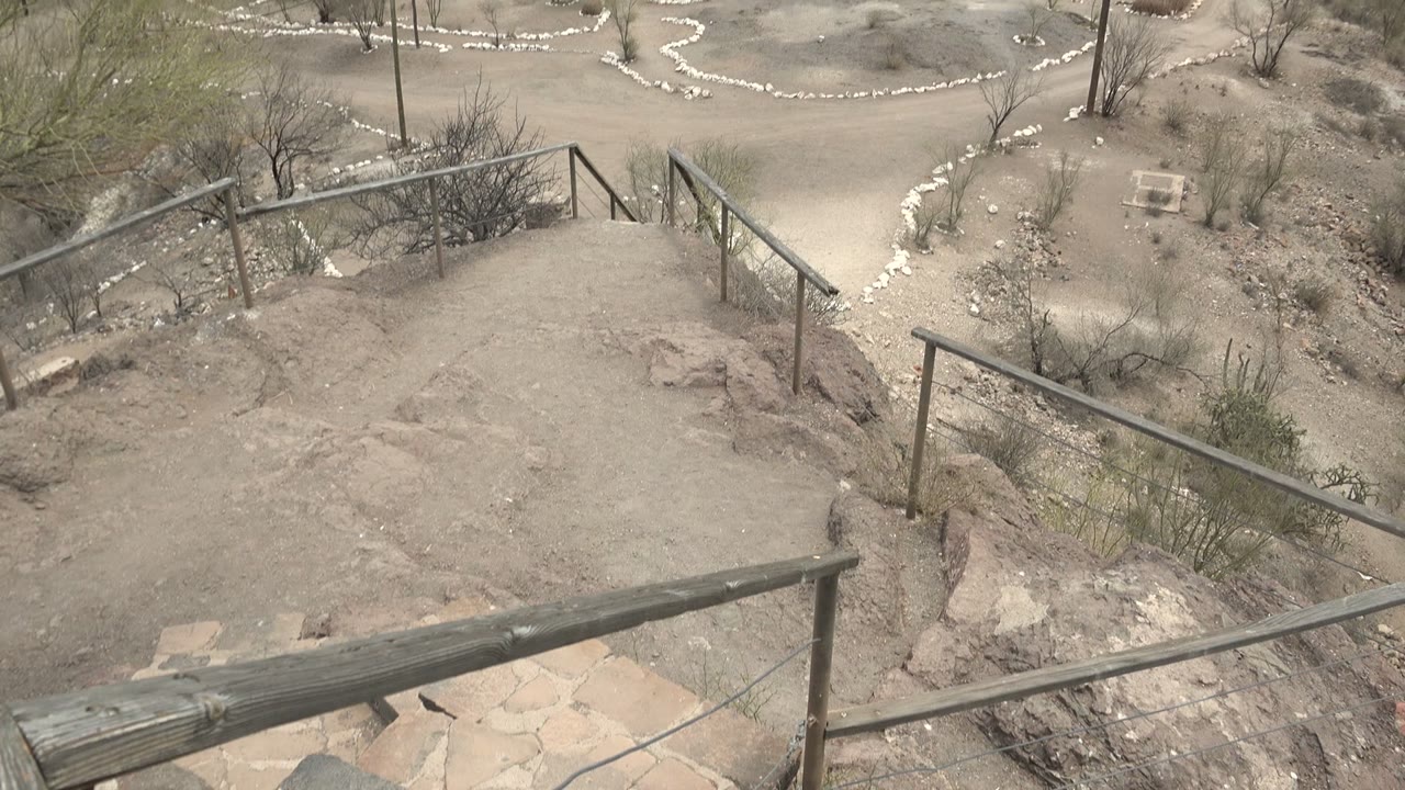The camera view over Mulege, Baja California Sur shows the stair landing and angled railings bordered by pale dirt, rocks, sparse shrubs, and no visible people.