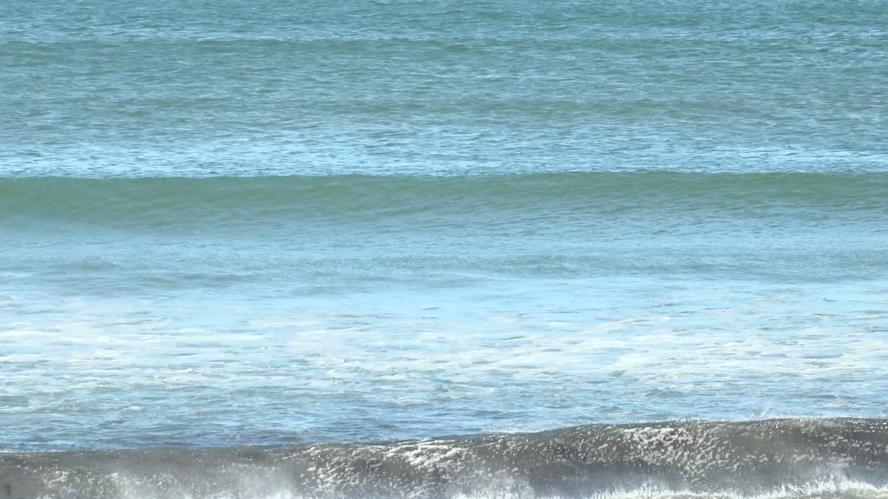 A low blue-green wave begins to form across the ocean surface at La Bocana, Baja California Sur, Mexico, with no visible people.