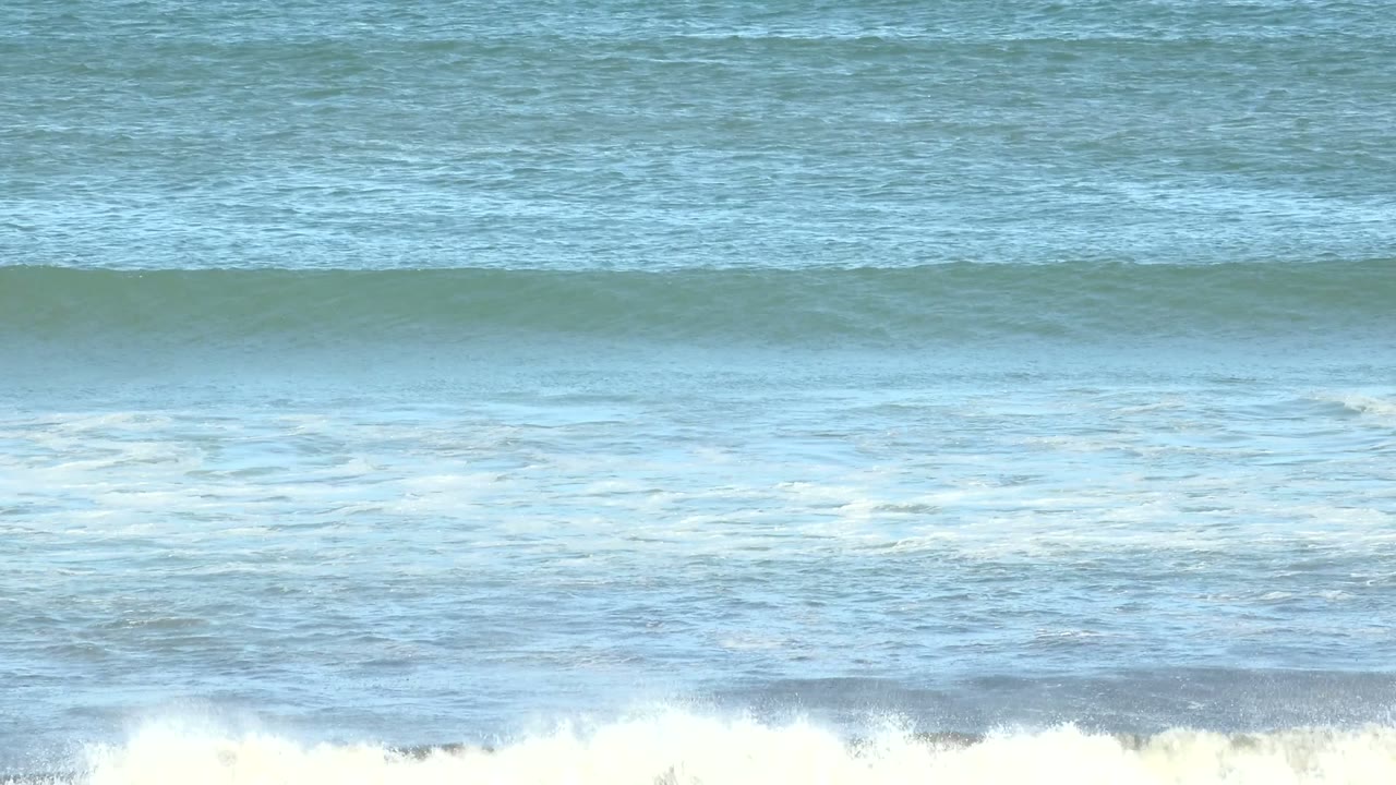 The wave breaks into white spray across the midground at La Bocana, with layered blue water behind it and no visible people.