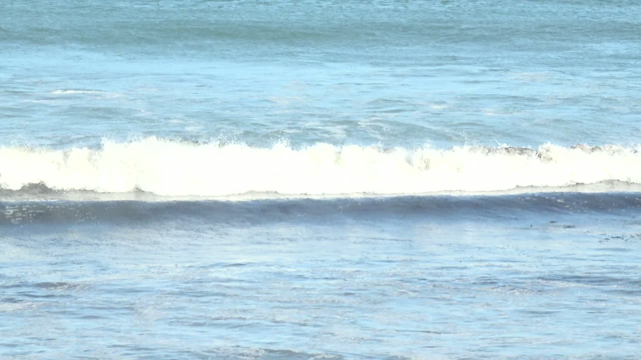 At 0:00 in La Bocana, Baja California Sur, blue ocean water forms horizontal surf bands with white foam breaking near the middle and dark rocks along the bottom, with no visible people.