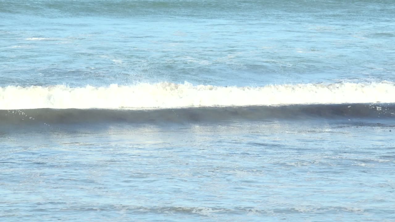 White surf spreads across blue water with rocks visible at the bottom.