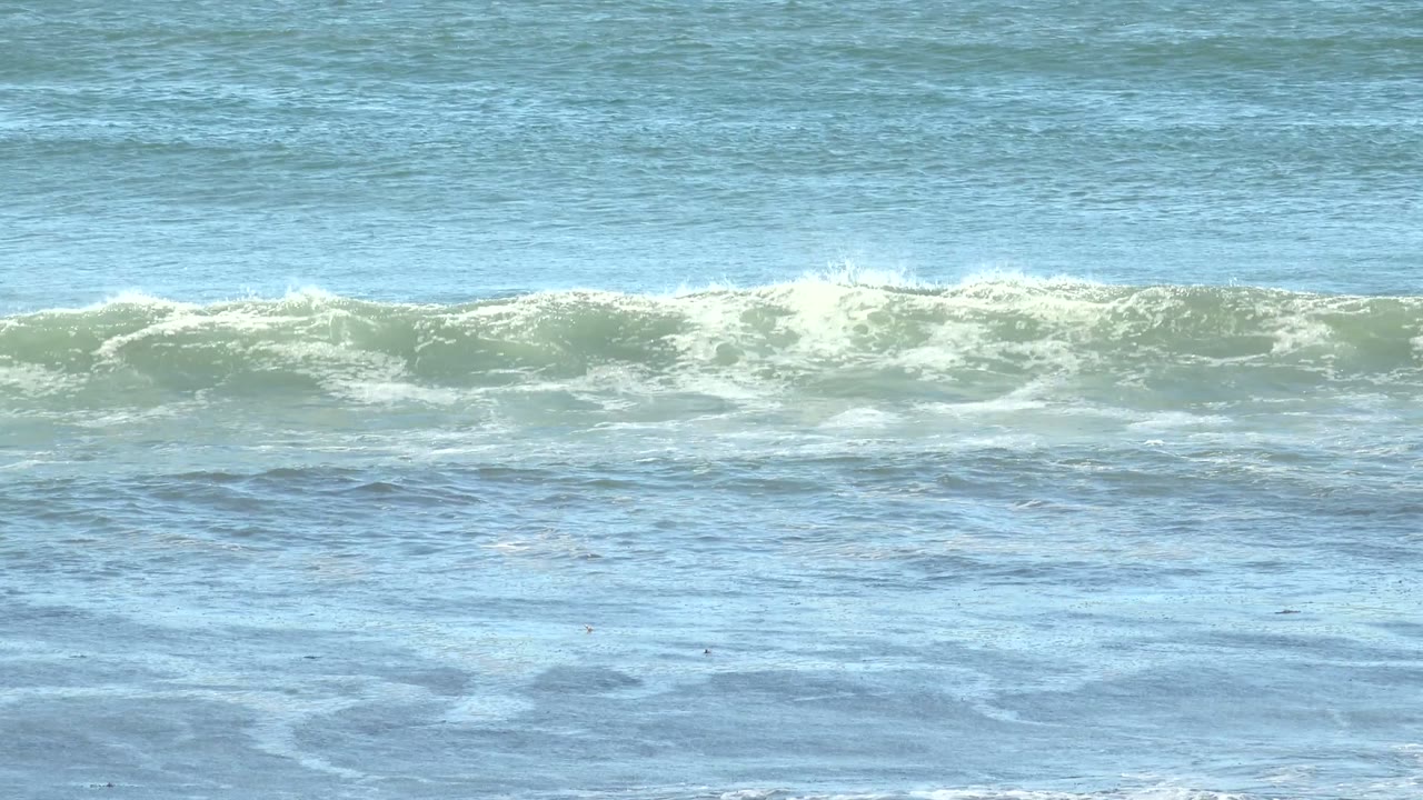 Breaking ocean wave with foam spreading across blue water