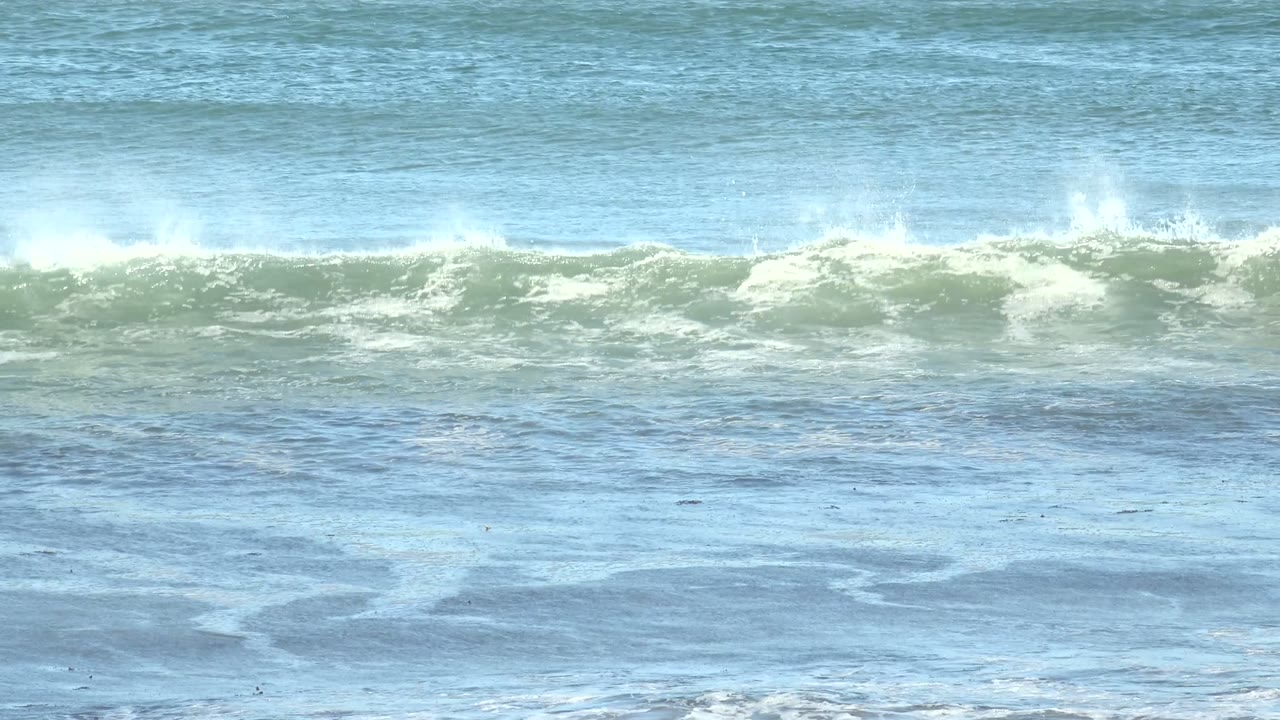 At La Bocana, Baja California Sur, white spray lifts from a long breaking wave near the top of the frame above calmer blue water below, with no visible people.