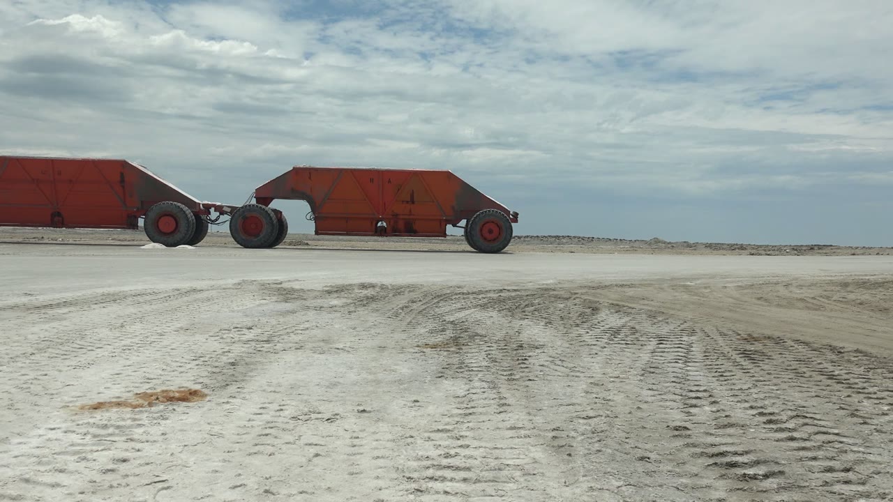 Red rusted vehicle on open sandy ground with tire marks.