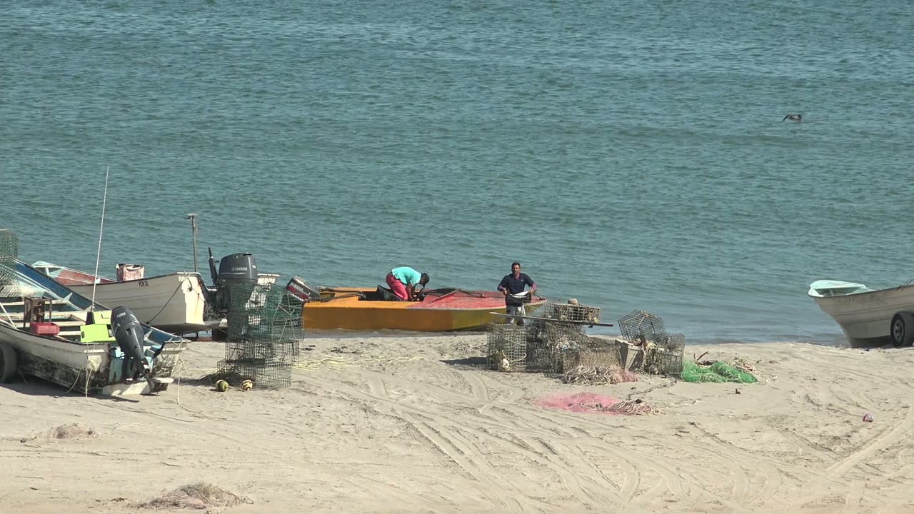 Fishermen work around an orange boat with nets and traps on the sand.