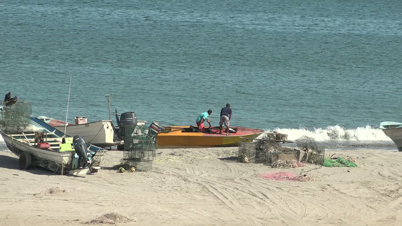 Two people stand on or beside an orange boat near gentle surf.