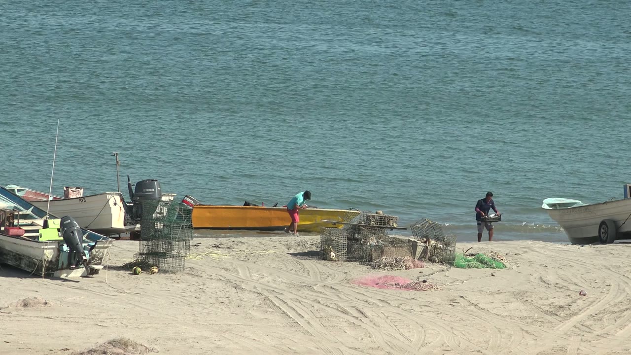 Person in a turquoise shirt moves near a yellow boat while another person stands by the water.