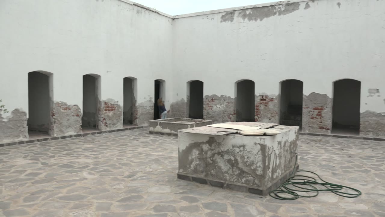 Person walking past arched doorways in a worn white stone courtyard.