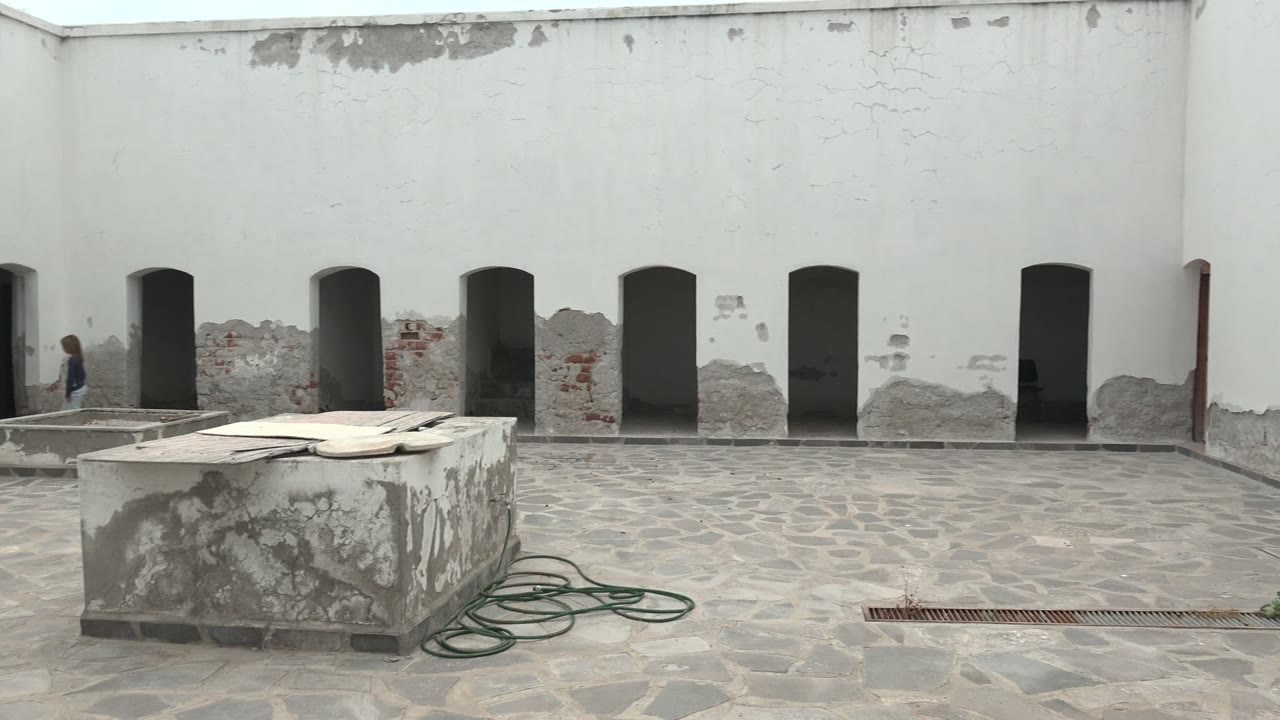 Courtyard with arched wall openings, stone table, hose, and worn plaster.