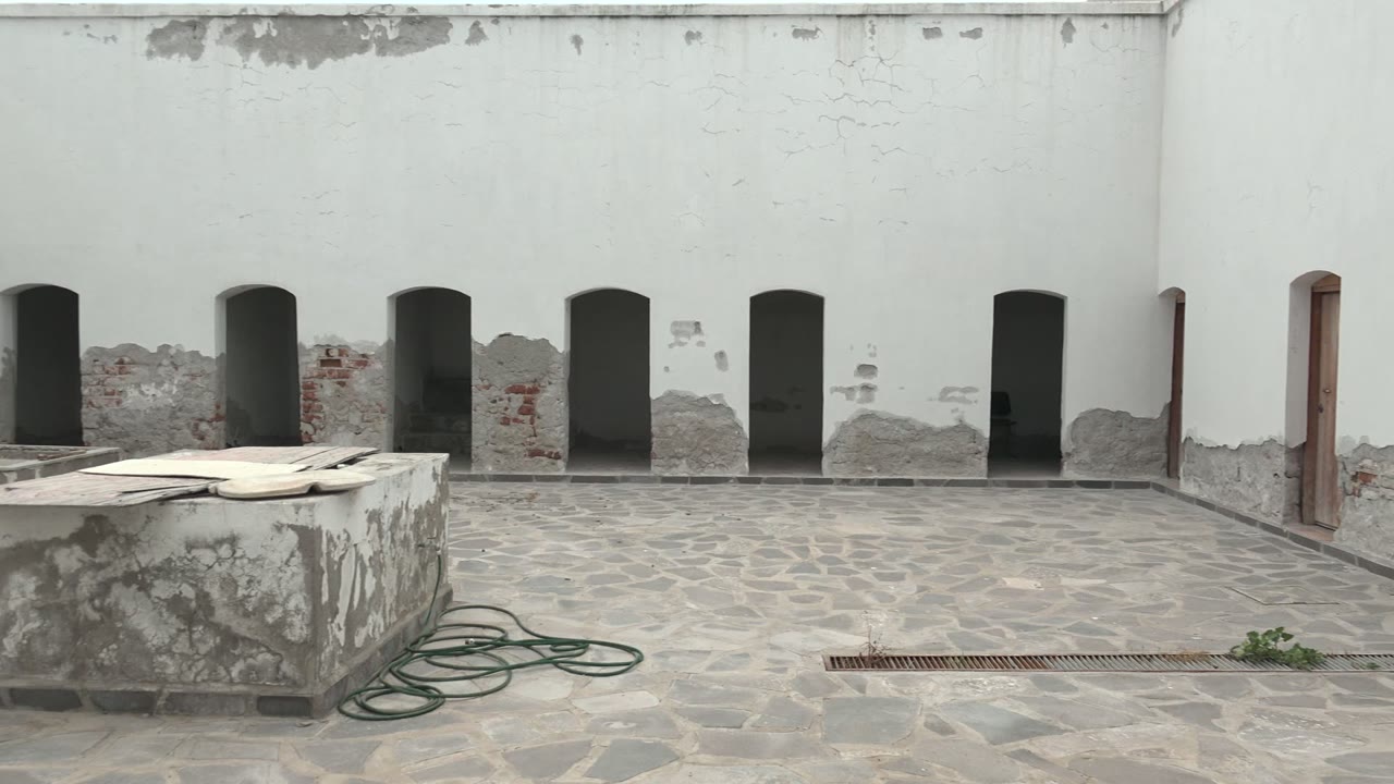 Weathered arched wall and courtyard floor with hose and drain.