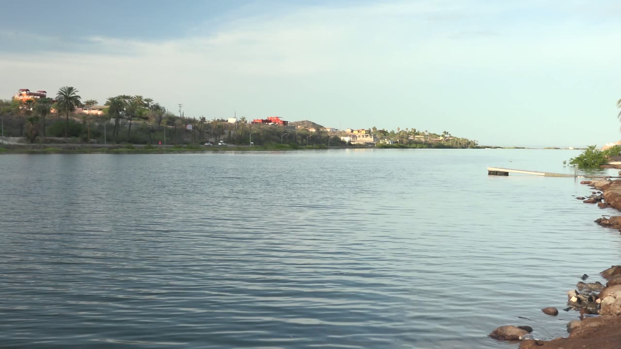 Rippling water with distant buildings and a small rocky edge at right.