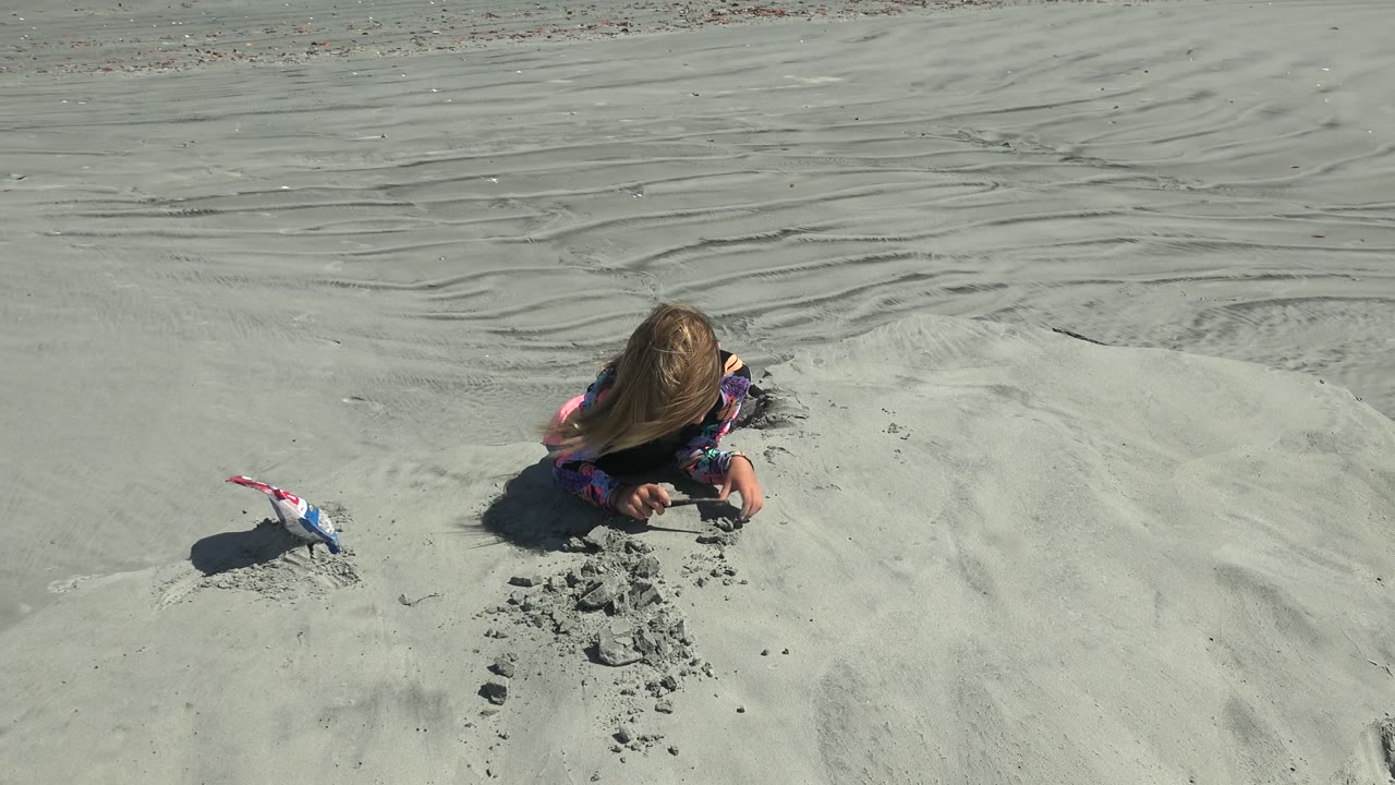 Girl on rippled sand with a toy shovel nearby.