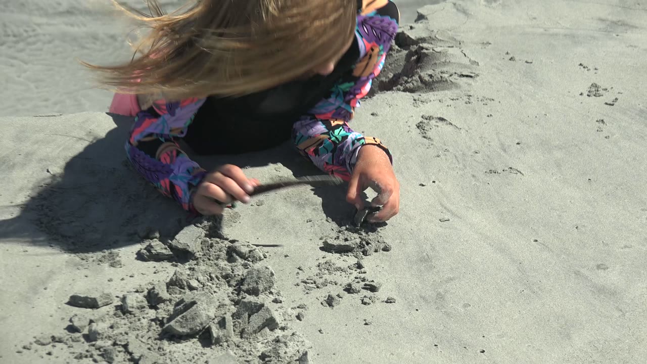 Child's hands near broken sand clumps on a sunlit beach surface.