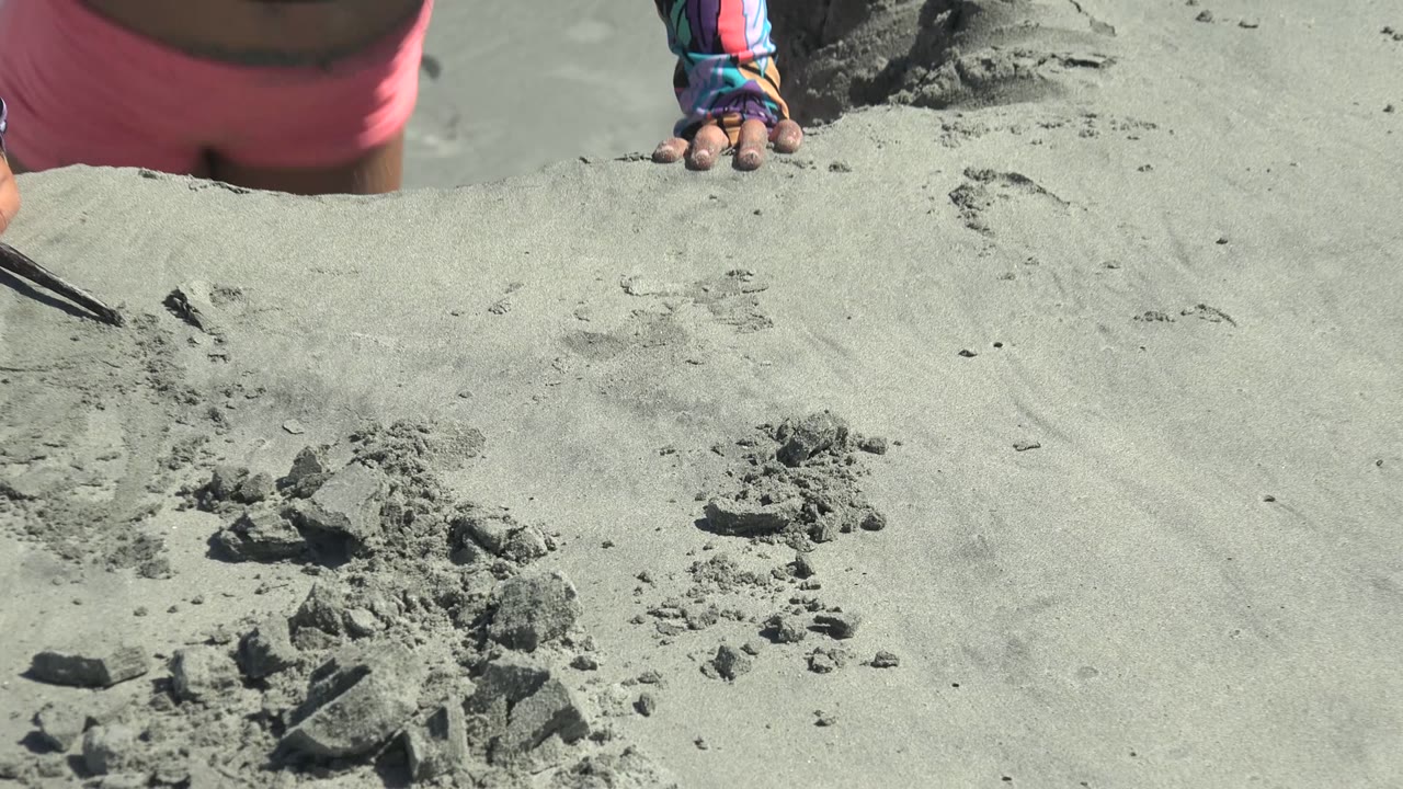 Only part of the child is visible at the top of the frame in La Bocana, Baja California Sur, above scattered sand structures on the beach.