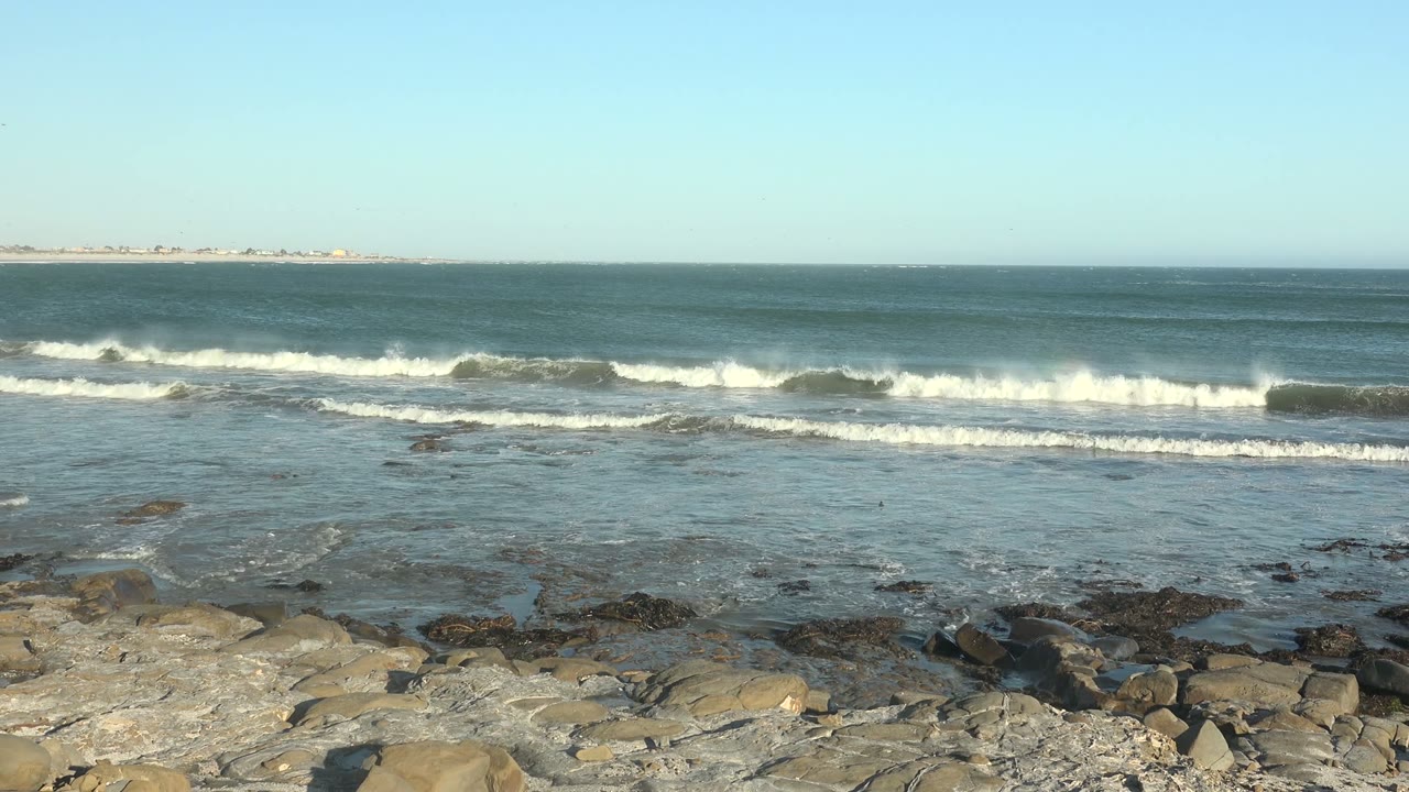 Whitecaps breaking across shallow water in front of a rocky shore.