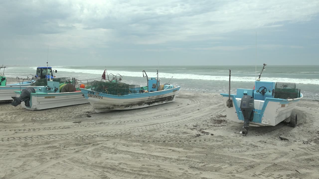 Fishing boats and gear on sand with ocean waves behind.