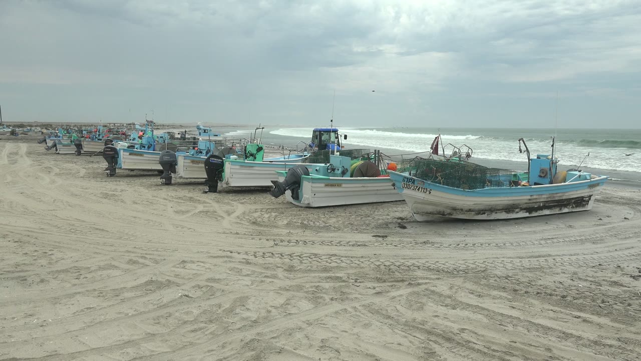 Beached fishing boats beside surf with a person walking nearby.