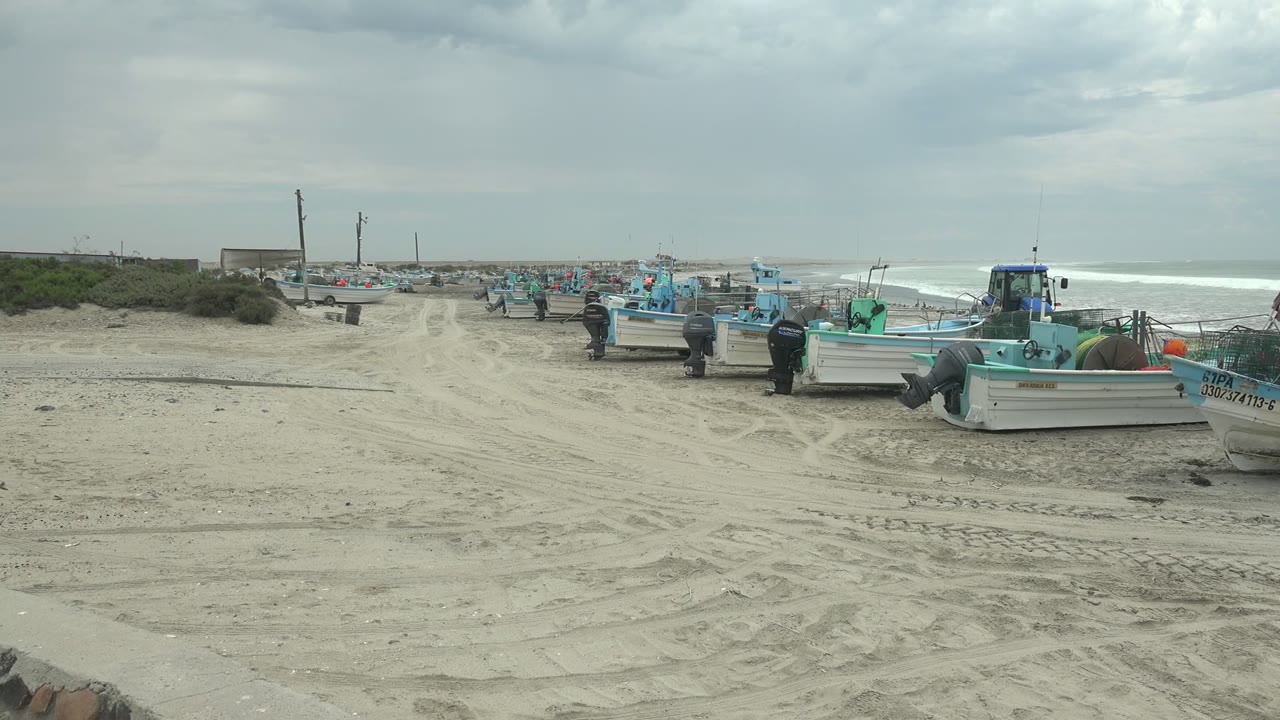 Small fishing boats and people on sand with surf in background.