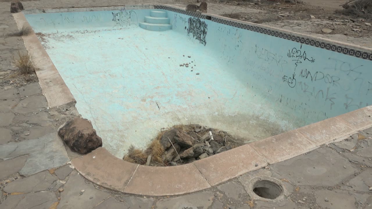 The pool corner in Mulege, Baja California Sur shows shallow steps, faded blue interior walls, graffiti, dry ground beyond the rim, and no visible people.