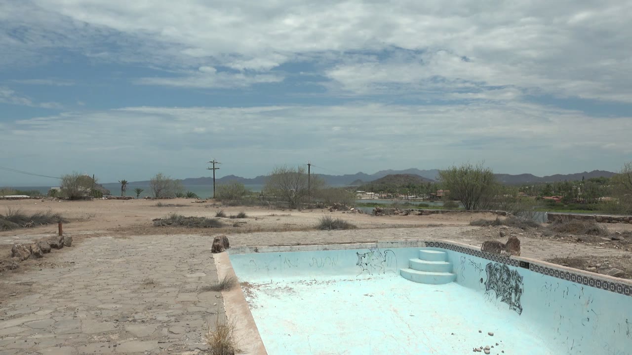 Abandoned empty pool with desert shrubs and mountains beyond