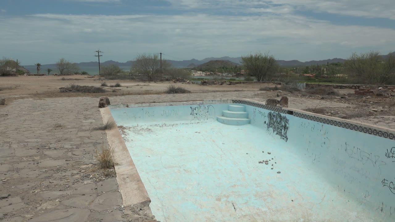Weathered empty pool with graffiti and desert hills beyond.