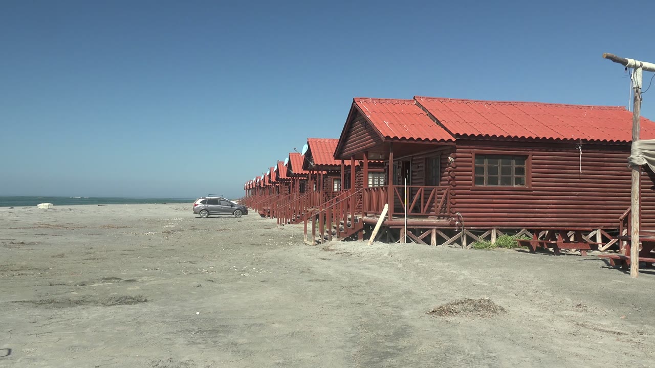 Cabin row on sandy beach with car near ocean