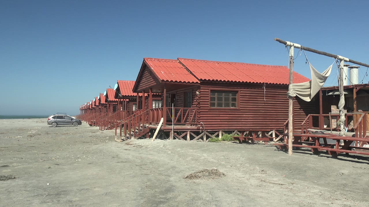 Row of red beach huts on sand with a white car in the background