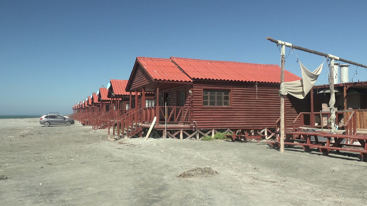 Third frame showing the red-roofed wooden huts extending into the distance in La Bocana, with the car still left of the buildings and no visible people.