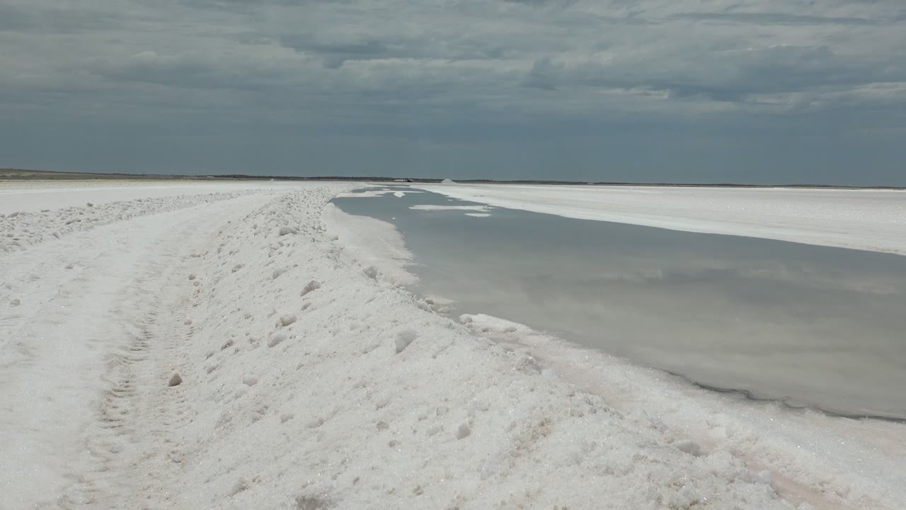 Footprinted white path curving beside gray water and ice.
