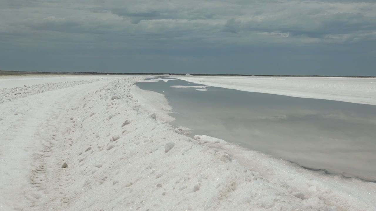 A white raised path borders a smooth gray water channel with patches of ice in Guerrero Negro, Baja California Sur, and no visible people.