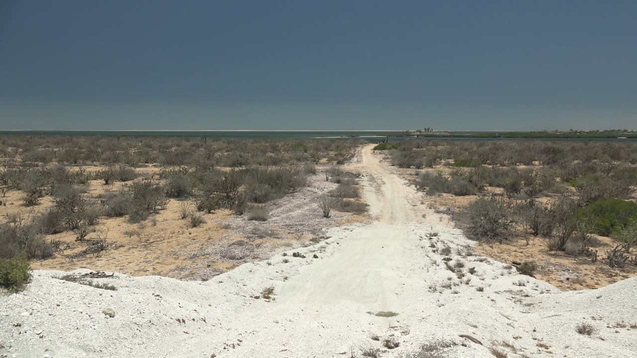 White rocky road foreground with dry scrub on both sides.