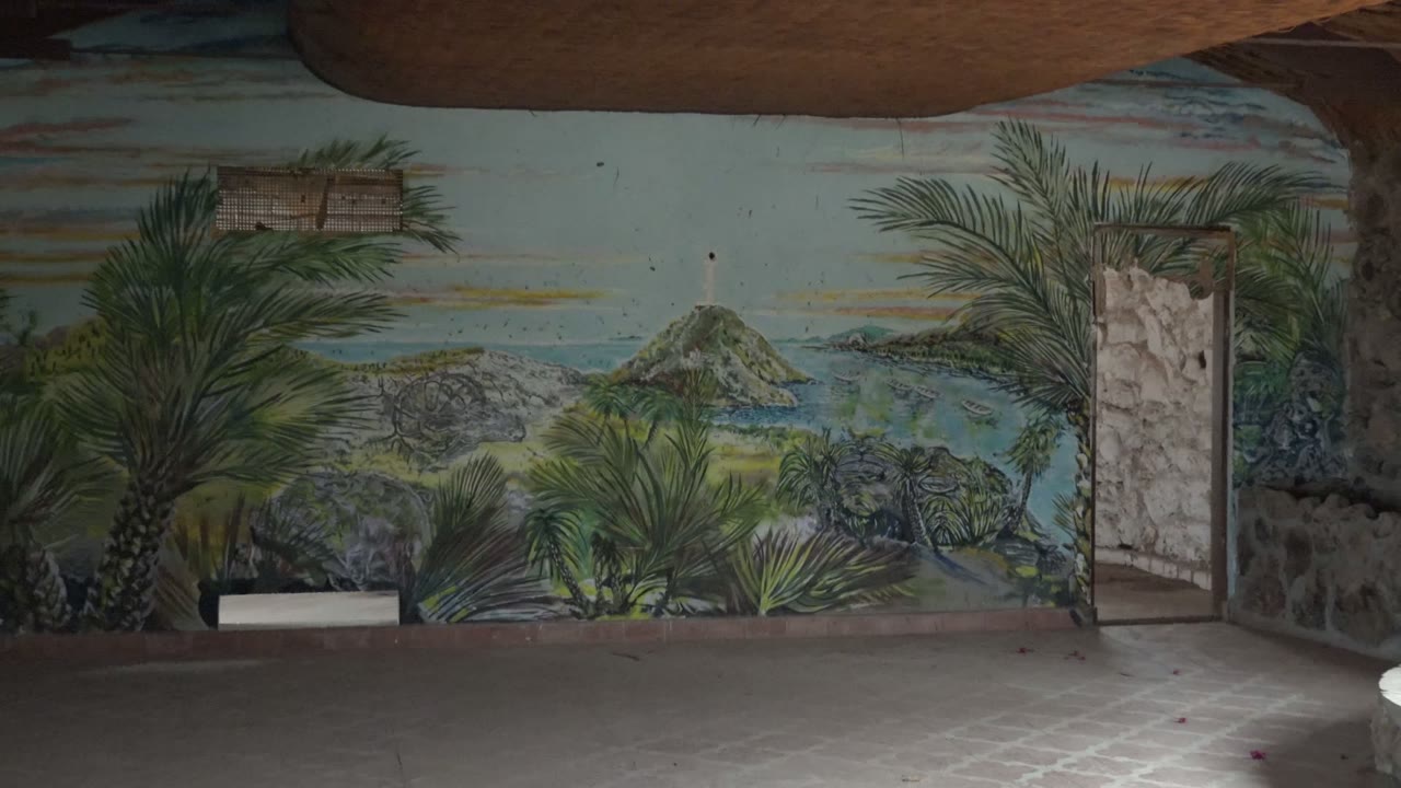 Interior mural wall with palm trees, painted island landscape, doorway, floor, and sink partly visible.