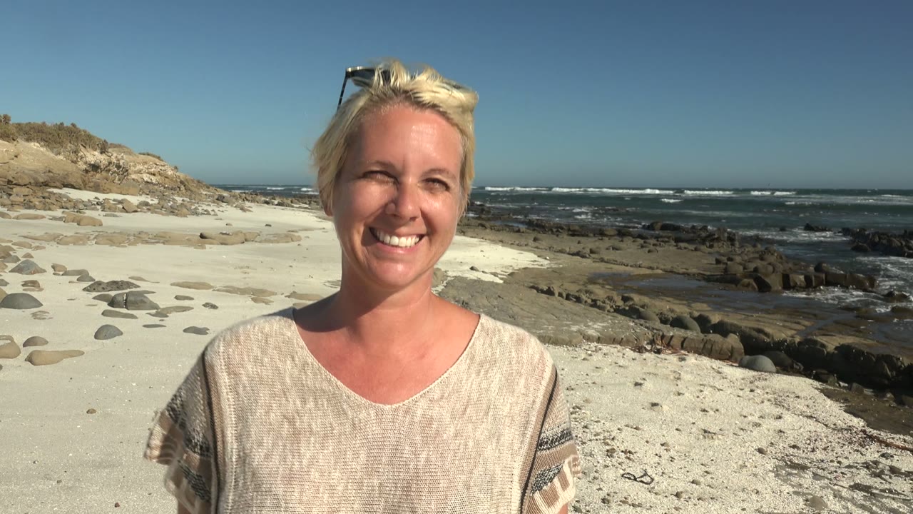 Smiling woman on beach with rocky shoreline and waves