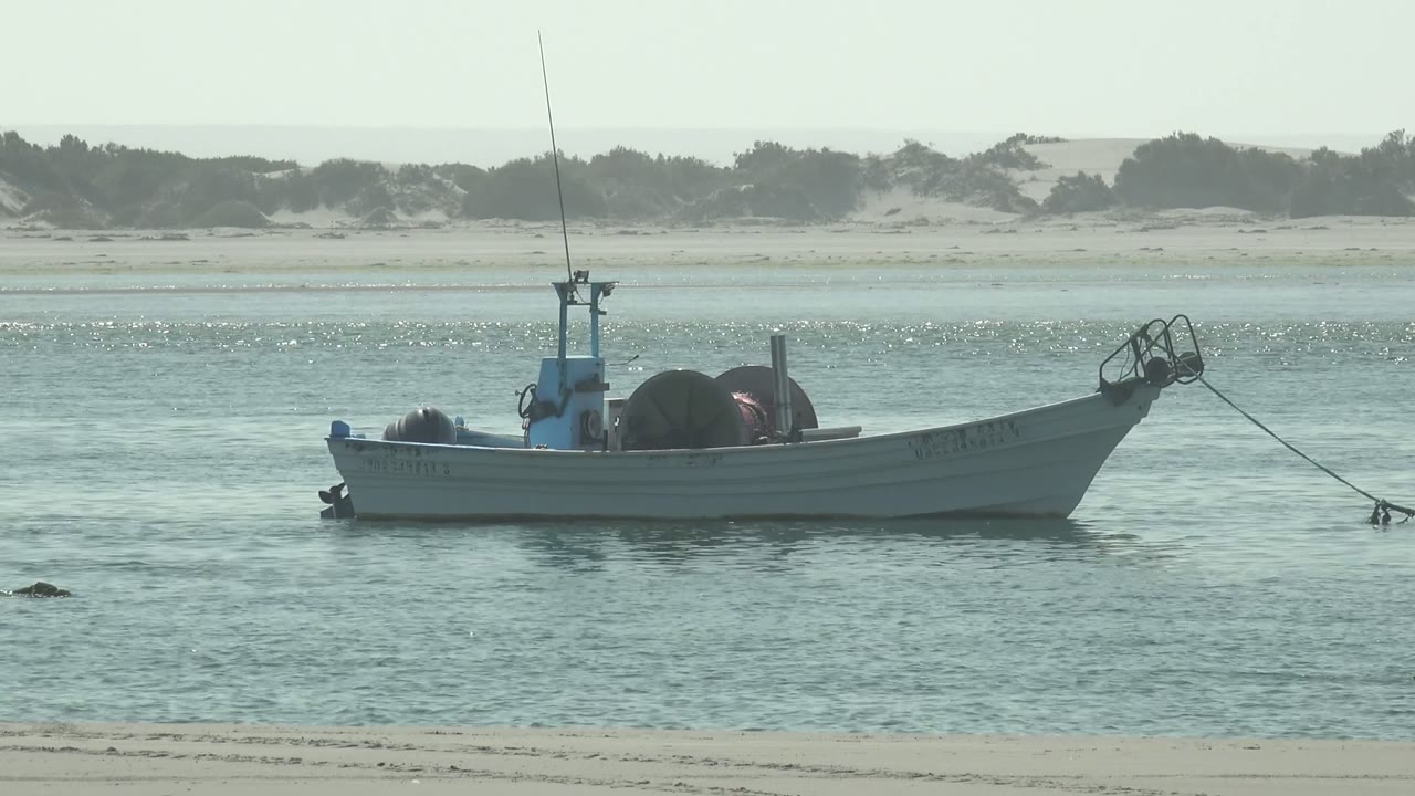 Anchored fishing boat with gear floating near low sandy dunes.