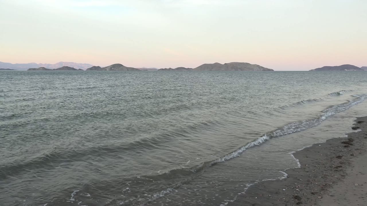 Small wave crest moving toward wet sand with low islands across the horizon.