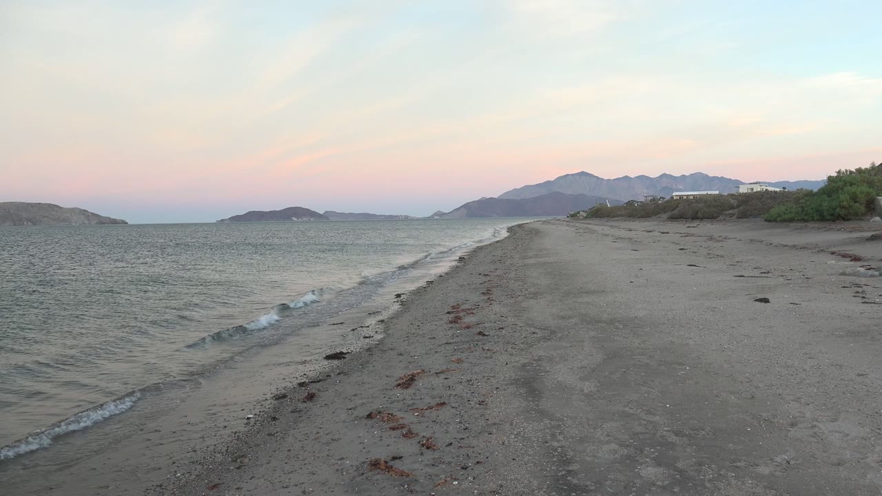 Dusk beach view with water, sand, seaweed, and mountain horizon