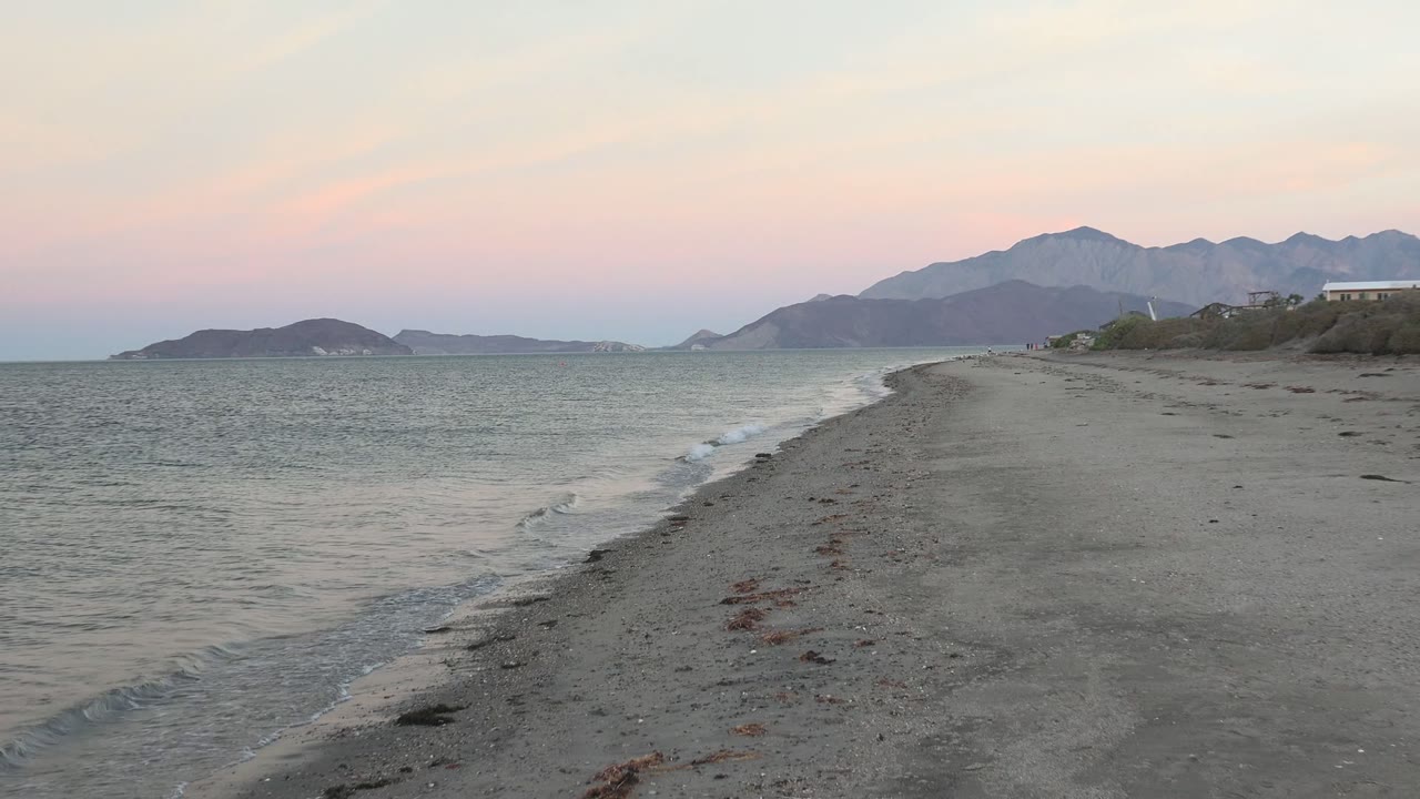 Low waves beside a sandy beach with mountains across the bay.