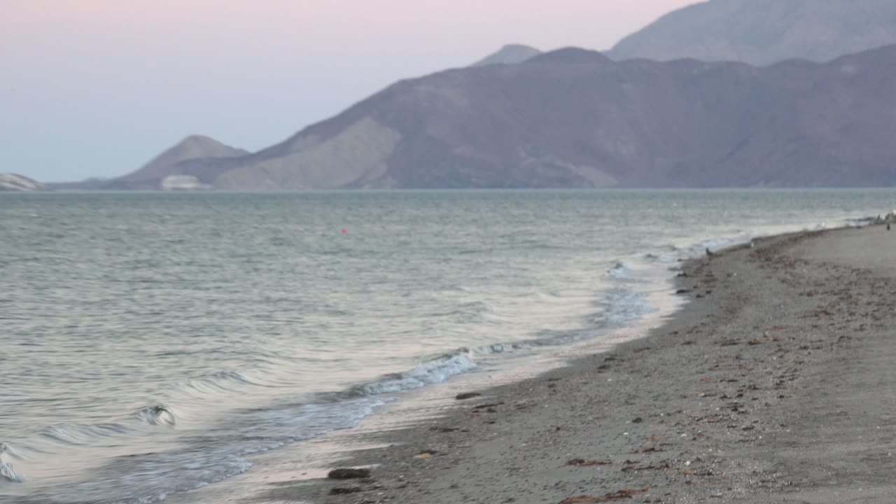 Narrow rocky shoreline with small waves breaking along both sides.