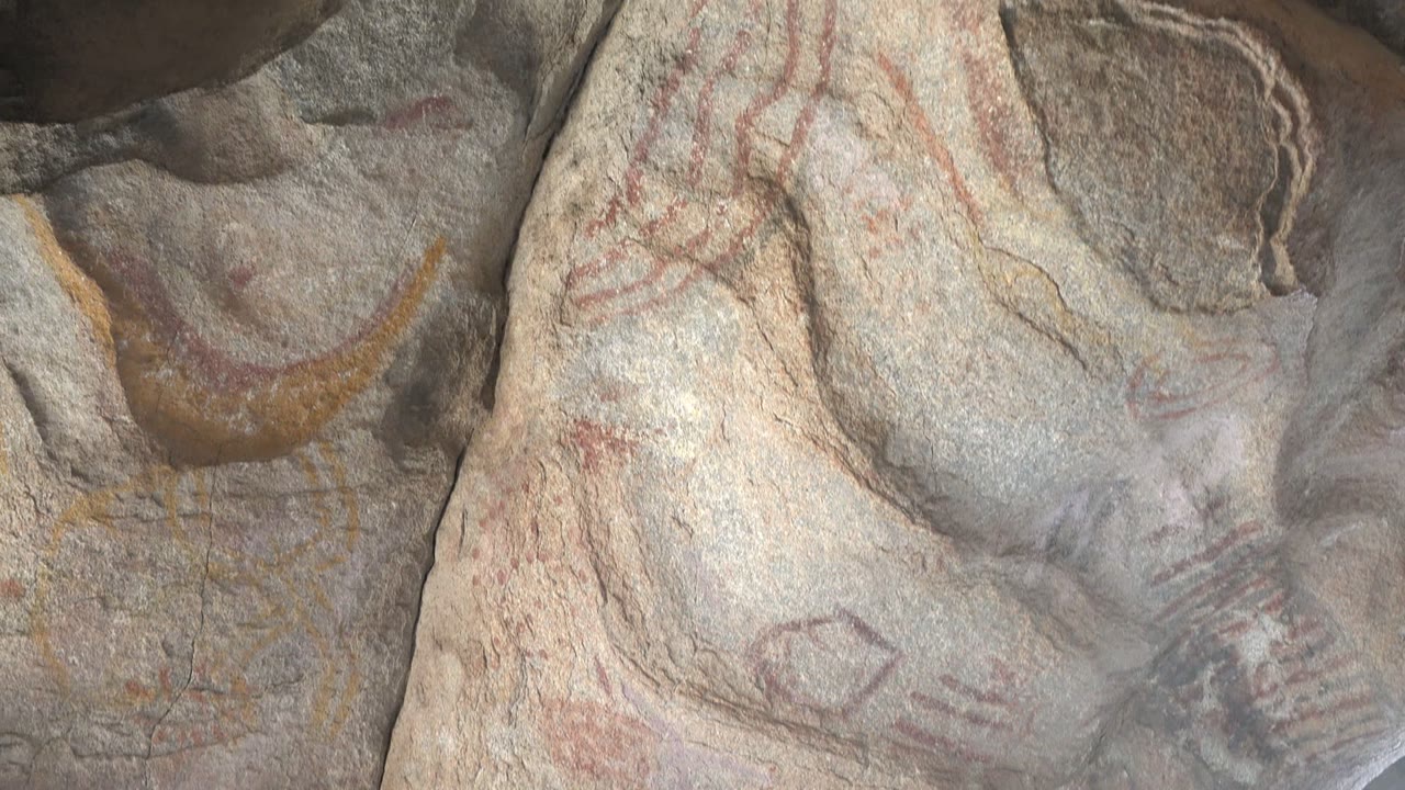 The frame holds on a textured Santa Rosalia stone surface with faint red pictographs, incised-looking shapes, yellow color, and no visible people.