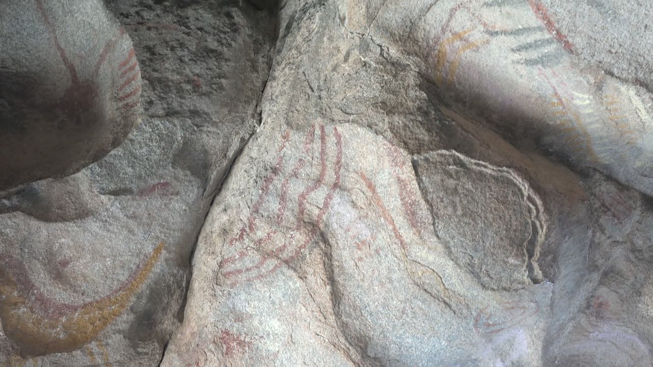 Opening frame of faded red handprints and pale pigment traces on gray rock art in Santa Rosalia, Baja California Sur, with no visible people.