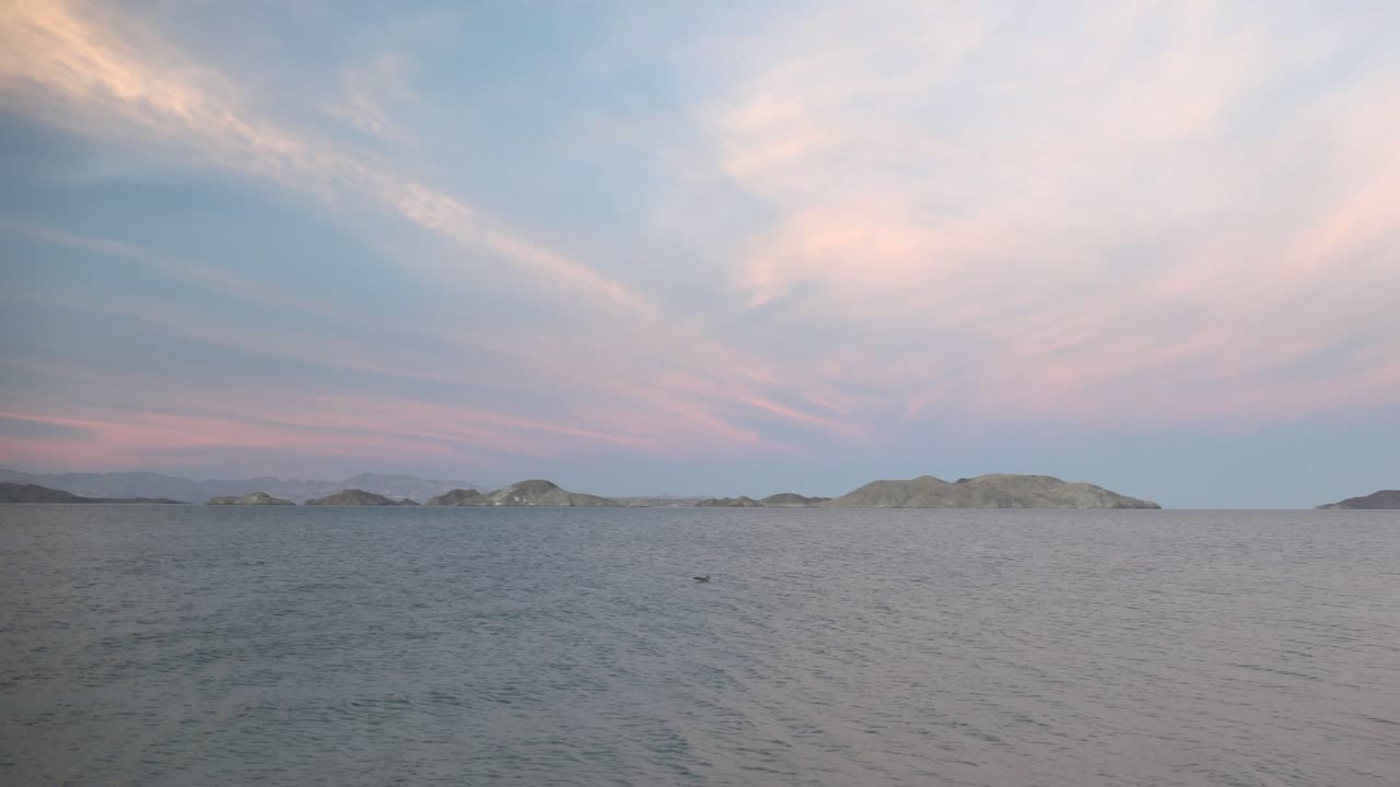 Open water and low islands beneath streaked pink sunset clouds