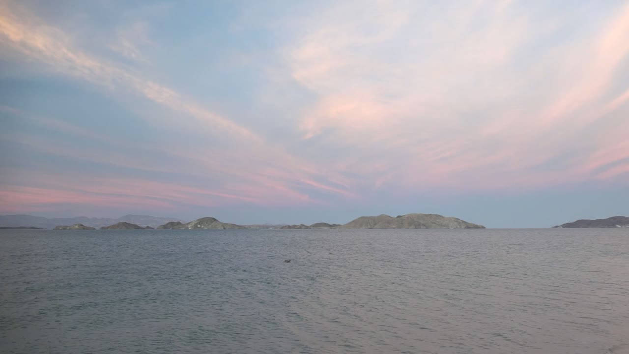 Calm coastal water in Bahia De Los Angeles, Mexico, with island silhouettes under a pastel pink and blue sky, and no visible people.