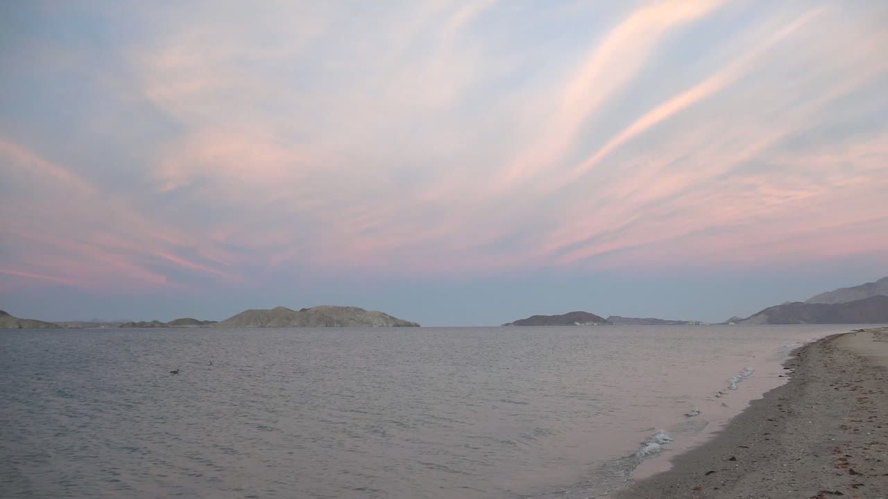 Sandy shoreline at dusk with calm water and low islands.