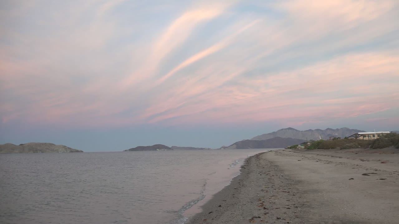 Gentle wave line along a sandy beach with islands beyond.