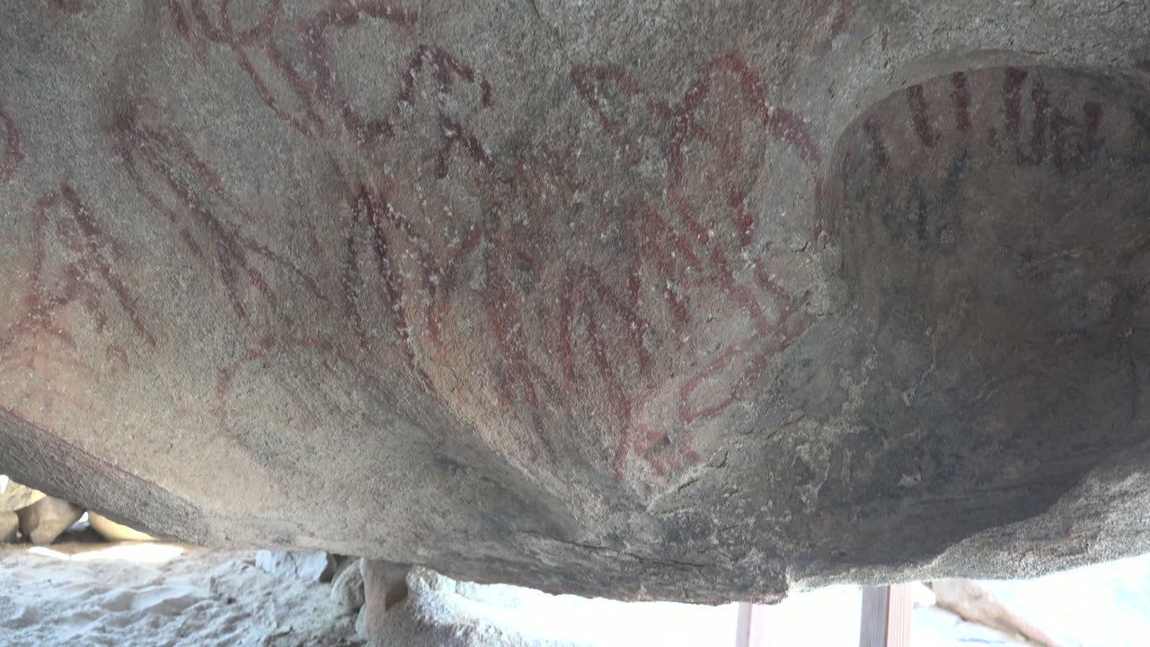 Faded red rock art beside a dark recess in gray stone