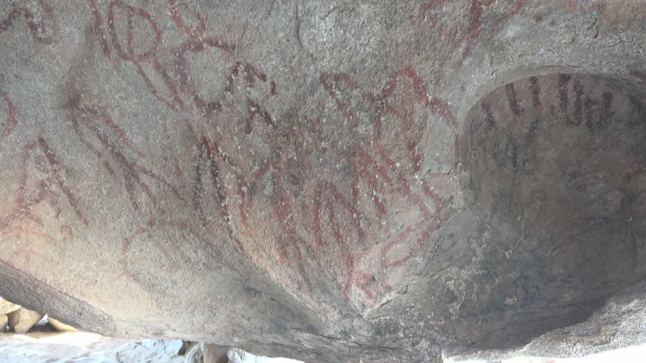 A close portion of the Santa Rosalia rock shelter shows red linear pictographs, circular marks, and weathered gray stone, with no visible people.